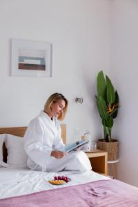 a woman sitting on a bed reading a book at Jasmine Hotel in São Pedro de Alva