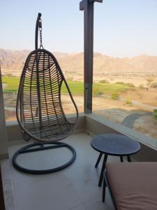 a swinging chair in front of a window with a table at Beautiful Golf & Sea View in As Sīfah