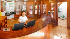 a man sitting at a desk with two laptops at Pousada do Norte in Jericoacoara