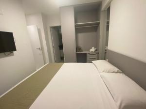 uma grande cama branca num quarto com uma televisão em Edifício Promenade II Apto 402-Mandi Hospitalidade em Maceió