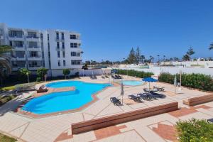 une grande piscine avec des chaises et un bâtiment dans l'établissement Loris Home playa ingles 50mt from Yumbo by luca properties gran canaria, à San Bartolomé