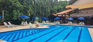 a swimming pool with chairs and blue umbrellas at Flat Incrível Amarilis dentro da Riviera São Lourenço - Apto duplex exclusivo 2 quartos 80m2, varanda privativa, enxoval, wifi, cozinha completa e serviço de praia in Riviera de São Lourenço