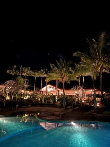 a swimming pool with palm trees at night at Rivland Resort in Païta
