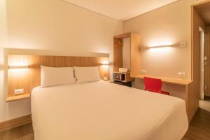 um quarto com uma cama branca e uma cadeira vermelha em Hotel Moov Porto Alegre em Porto Alegre