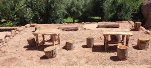 two tables and stumps in the dirt with trees at Maroc des Merveilles - Chez L'habitant in El Kelaa des Mgouna