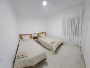 2 camas en una habitación con paredes y cortinas blancas en Apartamento Gómez, en Caravaca de la Cruz