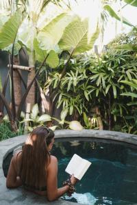 uma mulher sentada numa piscina a ler um livro em The Surf Shack - Stylish New 1 BR Studio w/ plunge pool em Uluwatu