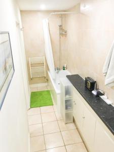Cozy bedroom in Clapton home في لندن: حمام أبيض مع حوض استحمام وسجادة خضراء
