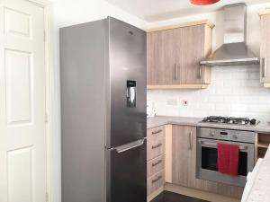 La cuisine est équipée d'un réfrigérateur en acier inoxydable et de placards en bois. dans l'établissement LovelyHome 4 family& Contractors, à Killingbeck