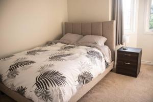 a bed with a black and white comforter and a night stand at Beautiful Home 5 Minutes from Ottawa Airport in Ottawa