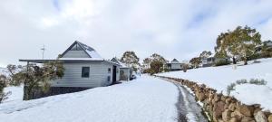 a house in the snow next to a stone wall at Adventist Alpine Village in Jindabyne