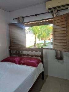 Schlafzimmer mit einem Fenster und einem Bett mit einem roten Kissen in der Unterkunft Casa em condomínio na praia de Paripueira AL in Paripueira
