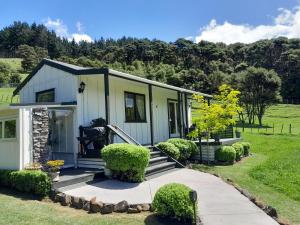 une petite maison avec une terrasse couverte et un jardin dans l'établissement Kuaotunu's Peebles Cottage, à Kuaotunu