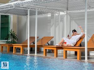 a woman sitting on benches next to a swimming pool at Buritel Hotel in Buriram