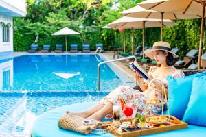 a woman sitting in a chair reading a book by a pool at Wyndham Garden Hoi An Cua Dai Beach in Hoi An