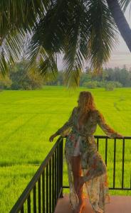 Eine Frau steht auf einem Balkon mit Blick auf ein Feld in der Unterkunft Man Guest Polonnaruwa in Polonnaruwa