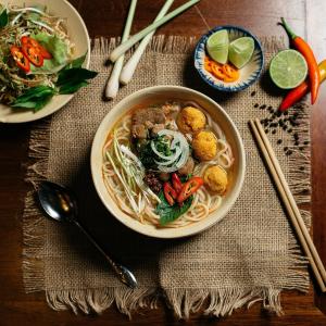 a bowl of food with noodles and vegetables on a table at HOUSE FOR ALL - CANTHO HOMESTAY in Can Tho