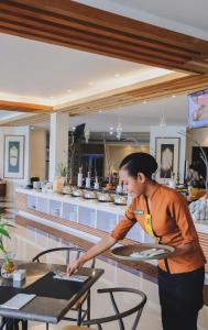 a woman is preparing a table in a restaurant at Hotel Suni Sentani in Jayapura