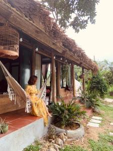 Eine Frau, die in einer Hängematte auf der Veranda eines Hauses sitzt. in der Unterkunft Nhà Gỗ An Trăm Tuổi - Chill Garden Lakeview in Hanoi