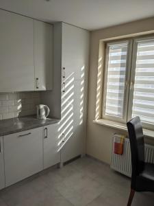 una cocina con armarios blancos y una silla junto a una ventana en Rigel Rooms, en Piotrków Trybunalski