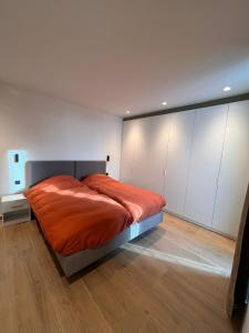 a bedroom with a bed with orange sheets and white cabinets at ApartHotel Dénia in Lochristi