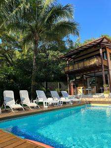 a pool with lounge chairs and a house with a palm tree at Moana Ilhabela in Ilhabela