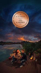 two people sitting at a table in front of a lake at Mártoni Resort & Restaurant in Szigetszentmárton