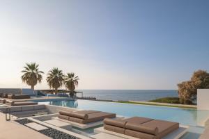 a swimming pool with lounge chairs and the ocean at Asea Villa, Spectacular right-on-the-beach Retreat, By ThinkVilla in Skaleta
