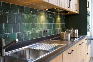 a kitchen with a stainless steel sink and green tiles at Les Hys de Verdenne in Marche-en-Famenne