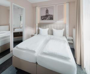 a white bedroom with a large white bed and a mirror at Villa Ney in Norderney