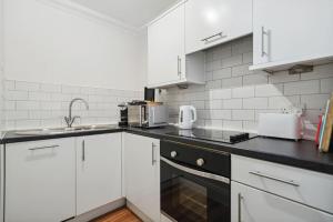 cocina con armarios blancos y encimera negra en (G2) Central 1 Bed Blythswood Flat en Glasgow