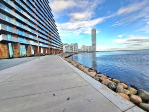 a sidewalk next to a body of water with buildings at Tranquil apartment with panorama view over ocean above 20th floor in Aarhus