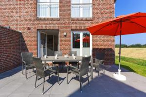een patio met een tafel en stoelen en een rode parasol bij Ferienhäuser Nordseetherme in Bensersiel