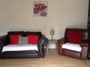 a living room with two leather chairs and red pillows at Darroch View Cottage in Invermoriston