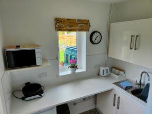 eine Küche mit einer Spüle, einer Mikrowelle und einem Fenster in der Unterkunft Self contained annexe in pretty Suffolk village in Bury Saint Edmunds