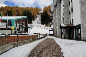 a snow covered street next to a building with a mountain at Casa Madesimo - Impianto sciistico e Parcheggio in Madesimo