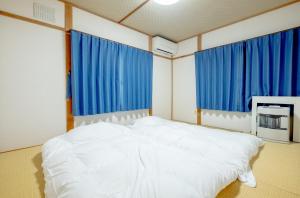 Cette chambre comprend un grand lit blanc et des rideaux bleus. dans l'établissement Furano Garden House - Vacation STAY 15463, à Furano