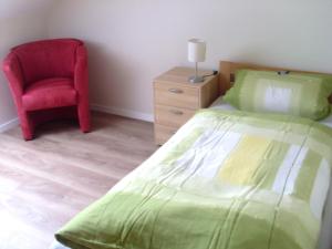 um quarto com uma cama verde e uma cadeira vermelha em Ferienwohnung am Waldrand em Schmallenberg