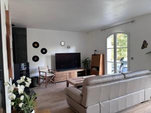 sala de estar con sofá y TV de pantalla plana en Les Persiennes, en Auvers-sur-Oise
