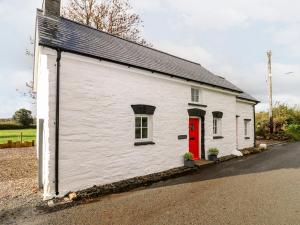 a small white building with a red door at Pensarngerrig in Llandysul