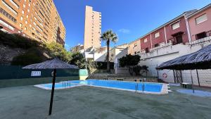 a swimming pool with an umbrella and some buildings at Bungalow Playa Poniente Benidorm in Benidorm