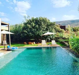 a swimming pool with two chairs and two umbrellas at Le Figuier du Lac Bin elouidane in Bine el Ouidane