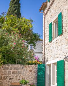 a stone house with green shutters and a stone wall at Revelin Hvar in Stari Grad