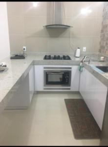 cocina blanca con fogones y microondas en Lindo Apartamento a beira Mar- Praia do Muta, en Porto Seguro