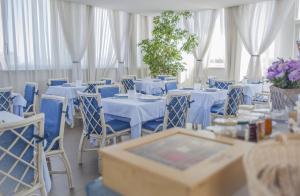 a room with white tables and blue chairs and flowers at Hotel Domus in Marina di Massa