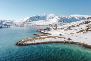 an island in a body of water with snow covered mountains at Serviced Farmhouse - Kvaløyvågen Gård in Kvaløya
