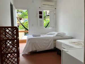 Duas camas num quarto branco com duas janelas em Tia Preta Pousada em Morro de São Paulo