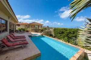 a swimming pool with chairs and a house at Beverly Hills Aruba in Palm-Eagle Beach