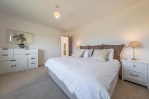 a white bedroom with a large bed and a dresser at Family water sports and cycling getaway - The Lake House in Ipswich