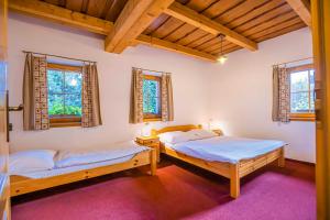 two beds in a room with wooden ceilings and windows at Holiday Raj in Bešeňová